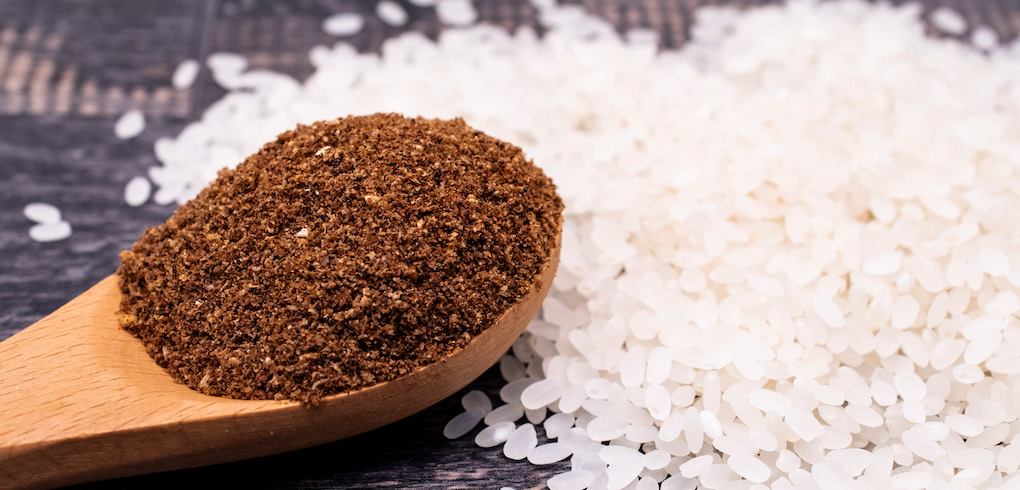 Scoop of rice bran in a wooden spoon with white rice in the background