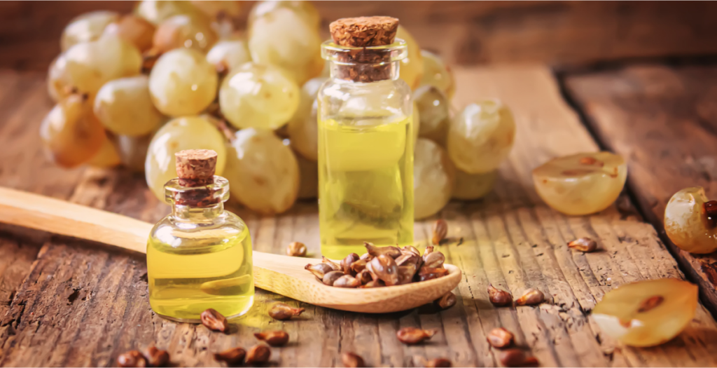 A wooden table with covered in grapes and grape seeds that sit inside a small wooden spoon. Small glass jars of grape seed oil sit on the table as well.